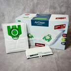 A package of white Miele AirClean 3D Efficiency U type vacuum bags with green detailing, including one bag visible in front of the box.