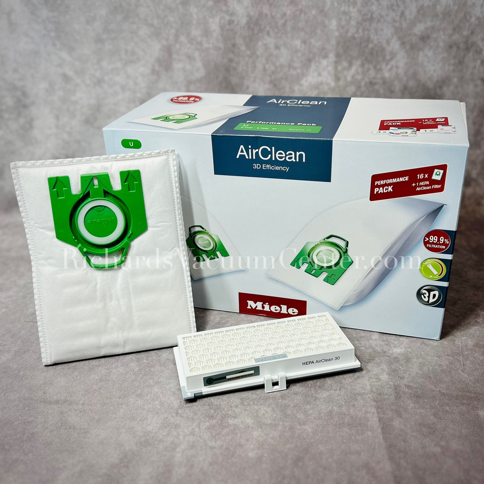 A package of white Miele AirClean 3D Efficiency U type vacuum bags with green detailing, including one bag visible in front of the box.