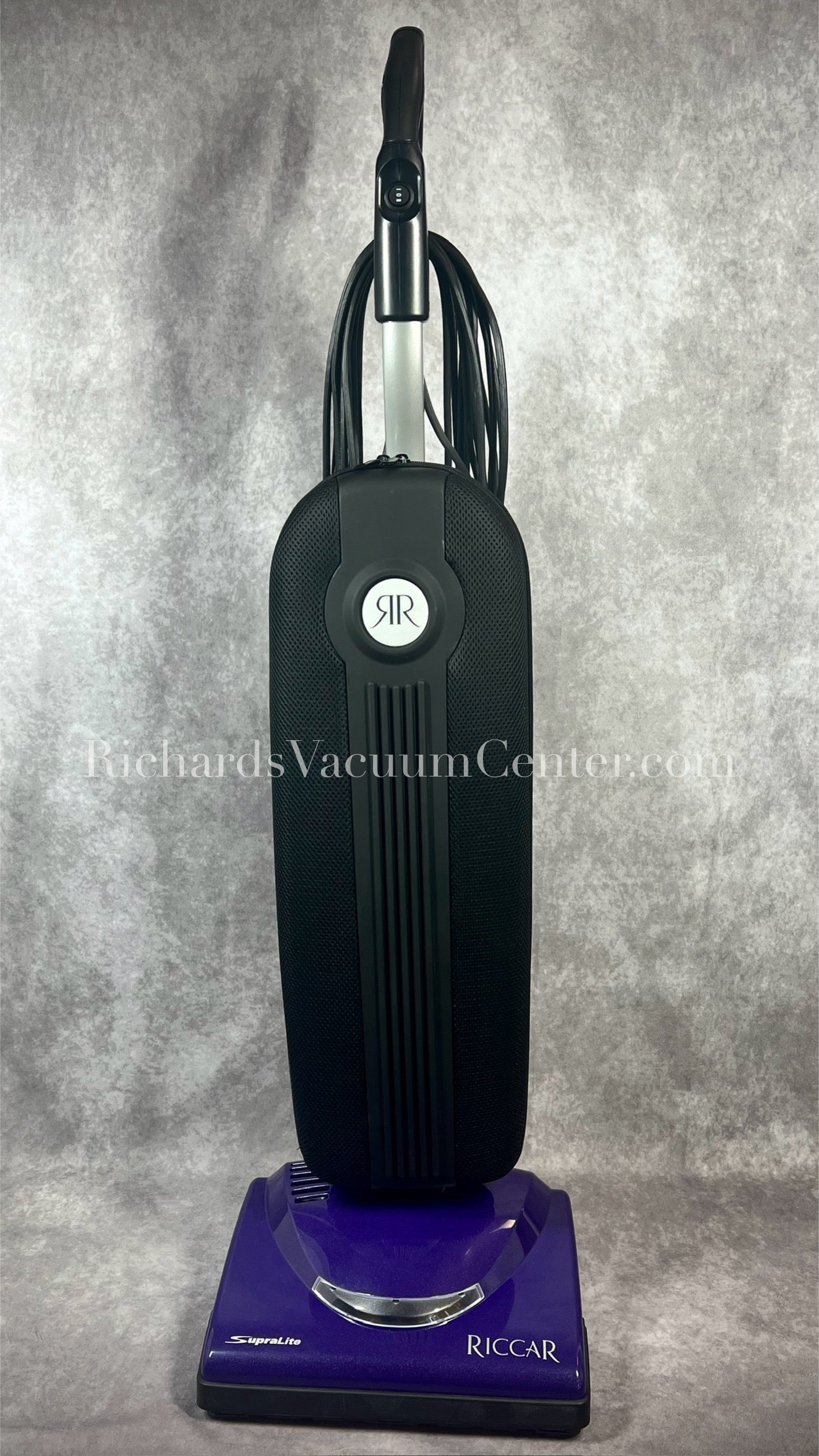 Upright Riccar vacuum cleaner in black color with a purple base, featuring a carrying handle and a power cord.